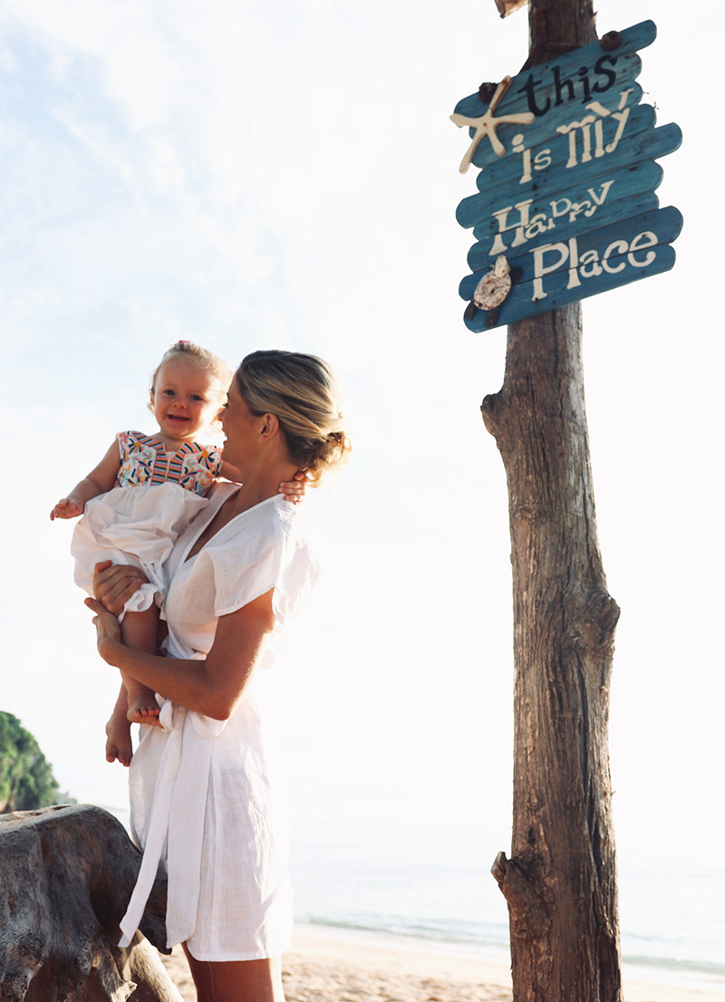 joanna hunt holding baby with this is my happy place sign on the beach